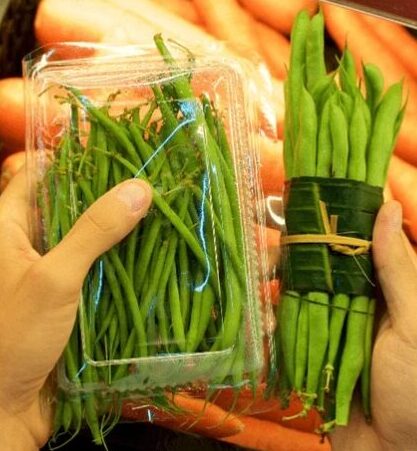 Hands holding a plastic container of vegetables and vegetables wrapped in a cloth. 