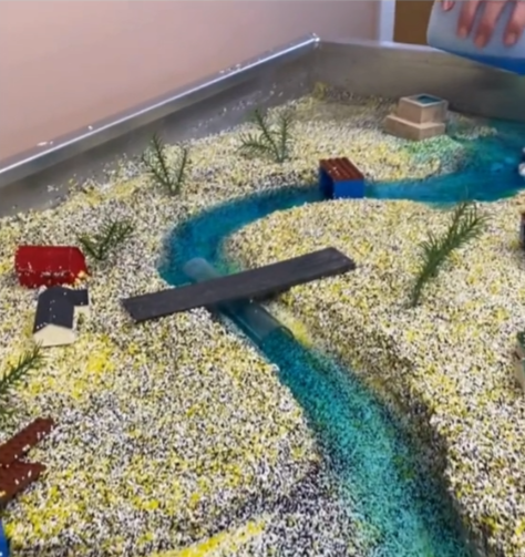 Model of a stream built with plastic media. Includes features such as buildings, bridges, vegetation and more. In the stream is a demonstrated pollution event - the blue coloring.